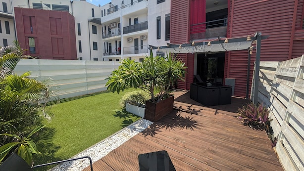 Una terraza en la azotea con mobiliario exterior, un pequeño jardín con plantas y vistas a edificios cercanos.