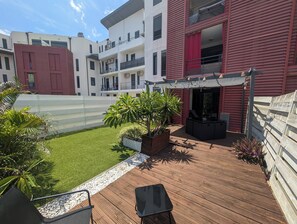 En tagterrasse med udendørs møbler, et lille haveområde med planter og udsigt til omkringliggende bygninger.