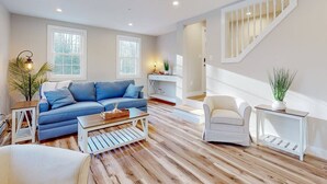 A modern living room with a blue sofa, white armchair, and wooden flooring. - Enchanting 3BR Farmhouse Retreat  Nature Getaway (Gorham)