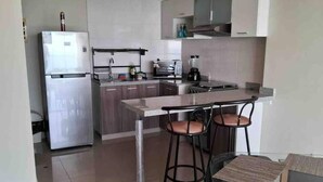 A modern kitchen with a refrigerator, microwave, toaster, and coffee maker. There is a bar stool and a small table with a placemat. - Beautiful apartment with balcony facing the sea (Lima)