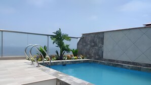 A rooftop swimming pool with a clear view of the ocean, surrounded by a tiled deck and potted plants. - Beautiful apartment with balcony facing the sea (Lima)