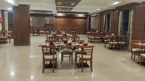 A spacious dining area with multiple tables and chairs, wooden paneling on the walls, and a fire extinguisher mounted on the wall. - HOTEL VIVOTEL (Surat)