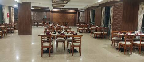 A spacious dining area with multiple tables and chairs, wooden paneling on the walls, and a fire extinguisher mounted on the wall.