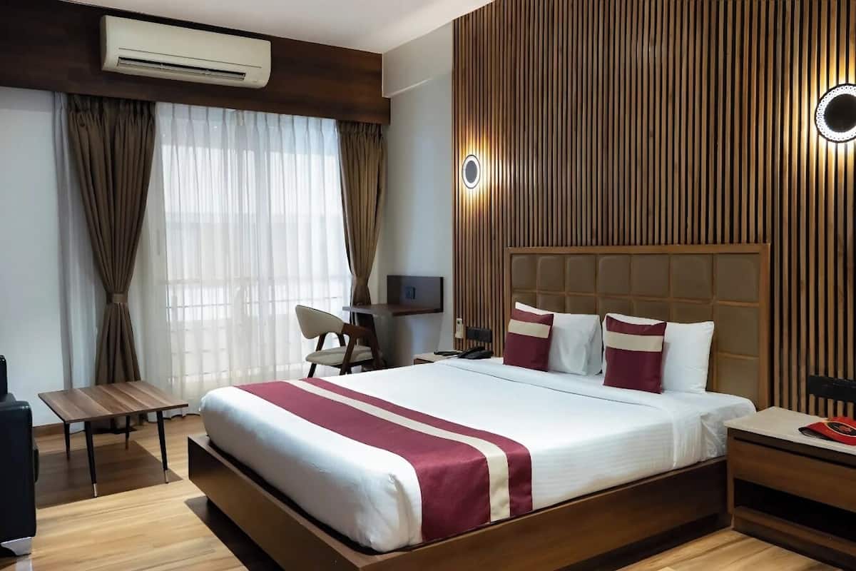 A modern hotel room with a large bed, a desk, a chair, and a nightstand.