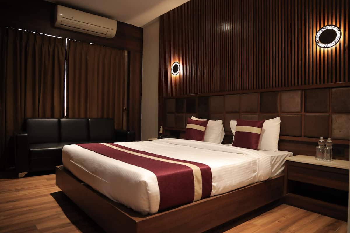A modern hotel room with a large bed, a dark leather sofa, and a wooden panel wall with circular light fixtures.