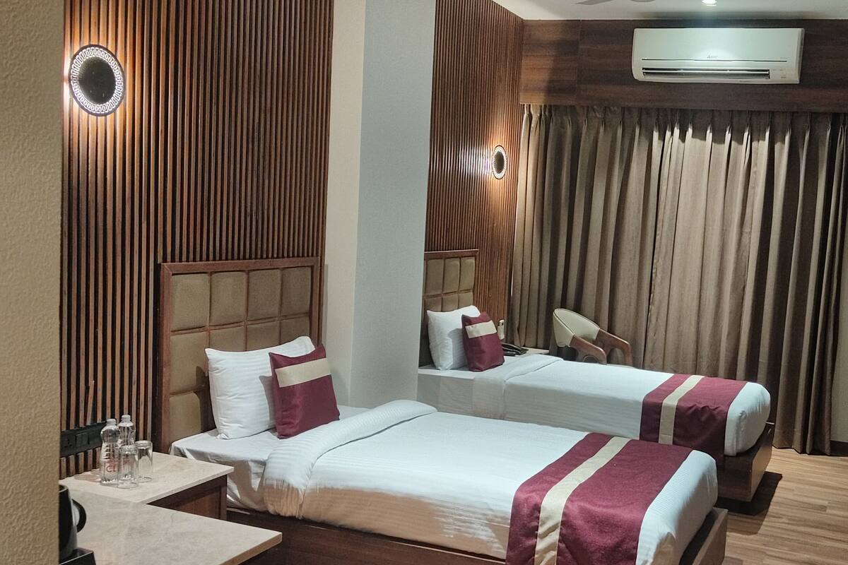 A hotel room with two beds, a small table, a chair, an air conditioning unit, and a television.