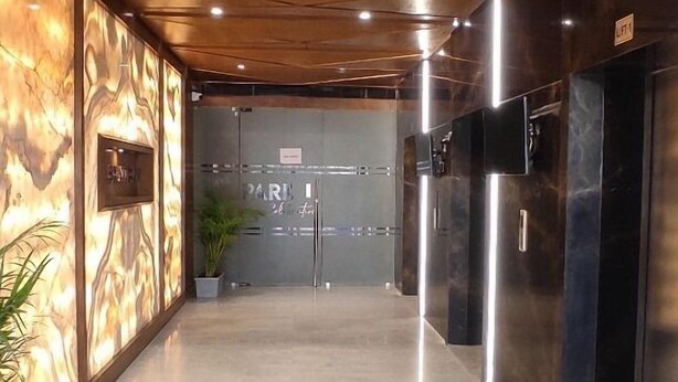 A hallway with a polished floor, a wooden ceiling, and a wall with a marble-like pattern. There are two doors with a sign above them. - HOTEL VIVOTEL (Surat)