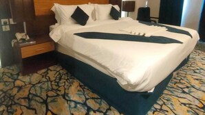 A hotel room with a large bed, a wooden headboard, a nightstand, and a patterned carpet. - Al Dera Hotel (Makkah)