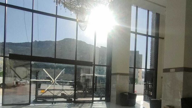 A spacious lobby with large windows, a chandelier, and a view of the mountains. - Al Dera Hotel (Makkah)