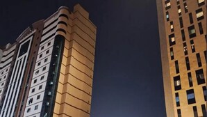 A nighttime view of a modern building with a prominent tower in the background. - Al Dera Hotel (Makkah)