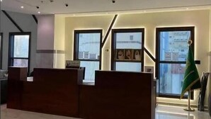 A modern reception area with a marble floor, wooden reception desk, and large windows offering views of the cityscape. - Al Dera Hotel (Makkah)