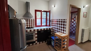 Een kleine keuken met een gasfornuis, een inbouwoven, een roestvrijstalen koelkast en een raam met rode kader.