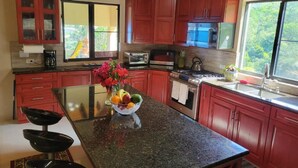 Una cocina con armarios rojos, encimera de granito, tostadora, cafetera y un tazón de fruta.