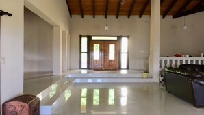 Un pasillo amplio con piso pulido, una puerta de madera al final y un sofá de cuero a la derecha.