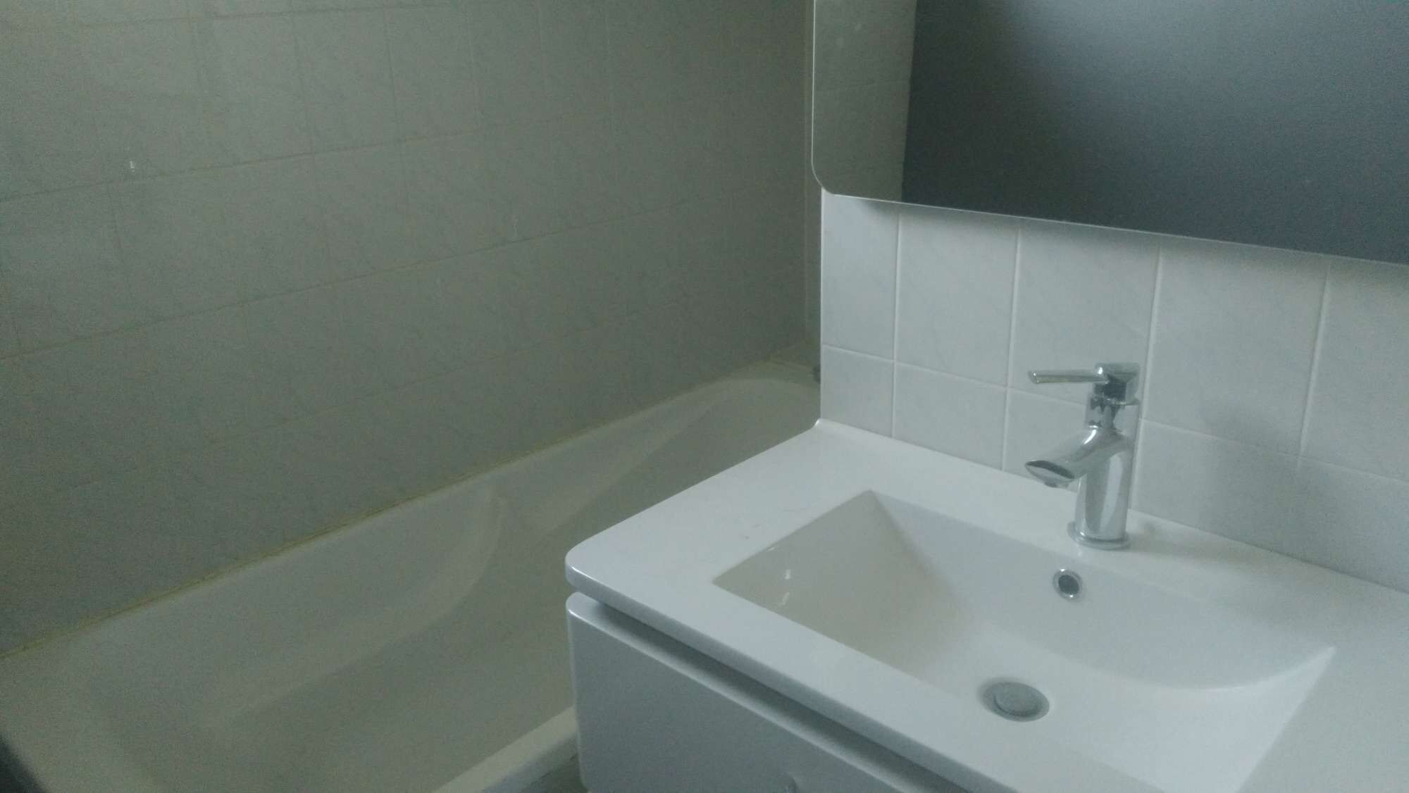 Een badkamer met een witte wastafel, een spiegel erboven en een bad.