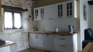 Een keuken met witte kastjes, een spoelbak, een fornuis en een raam met gordijnen.