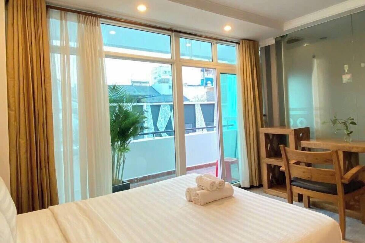 A hotel room with a large bed, a wooden desk, and a view of the outside.