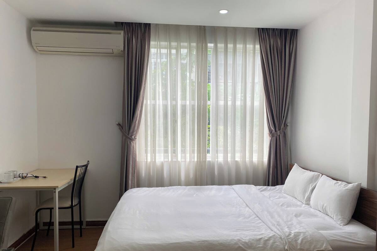 A hotel room with a bed, a desk, and an air conditioning unit.