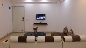 Een moderne woonkamer met een flatscreen televisie aan de wand, een bank met gestreepte kussens, een salontafel en een deur.