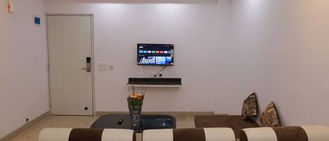 A modern living room with a flat-screen TV mounted on the wall, a sofa with patterned cushions, a coffee table, and a door.