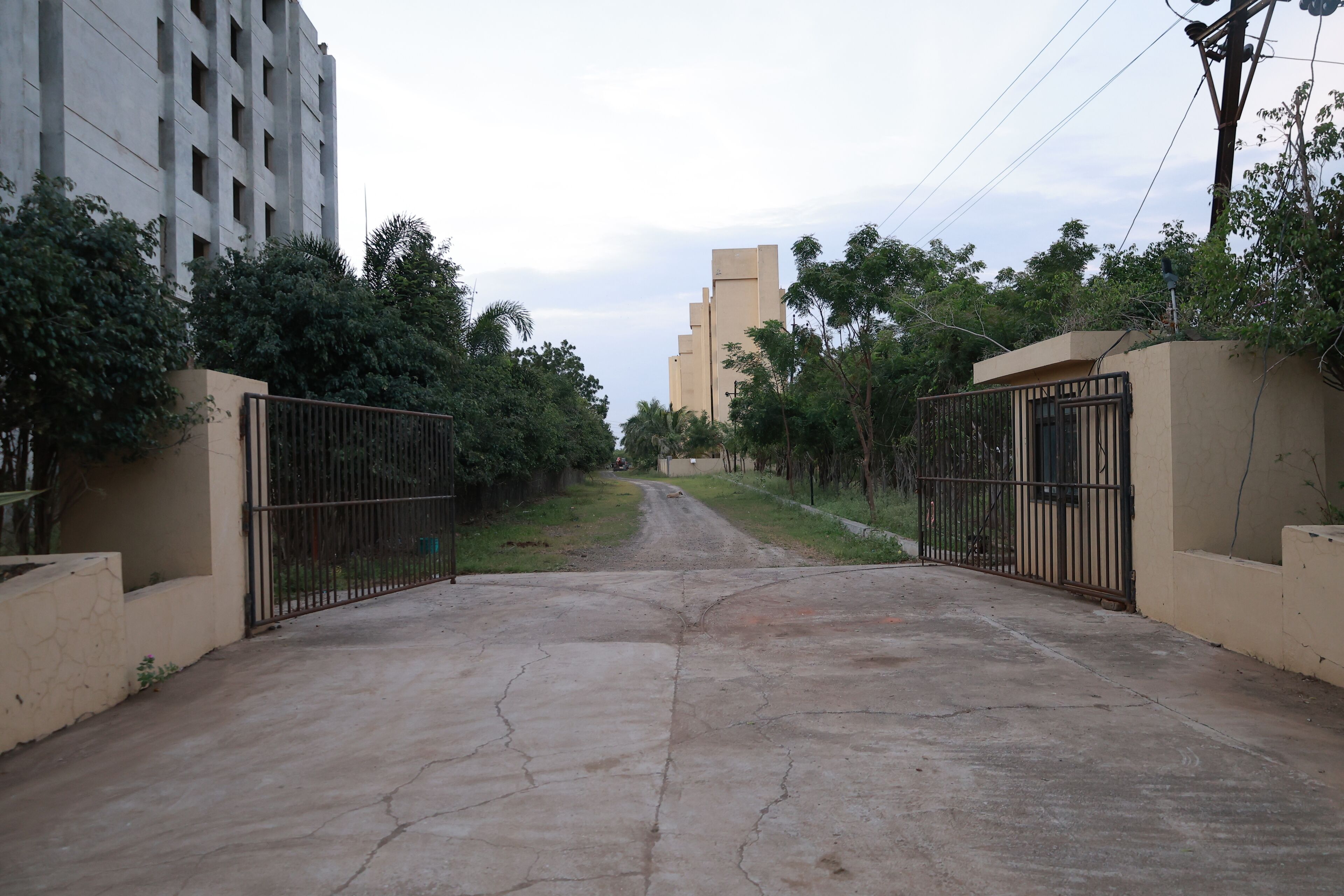 A gated entrance to a residential area with a concrete road leading to a tall building.