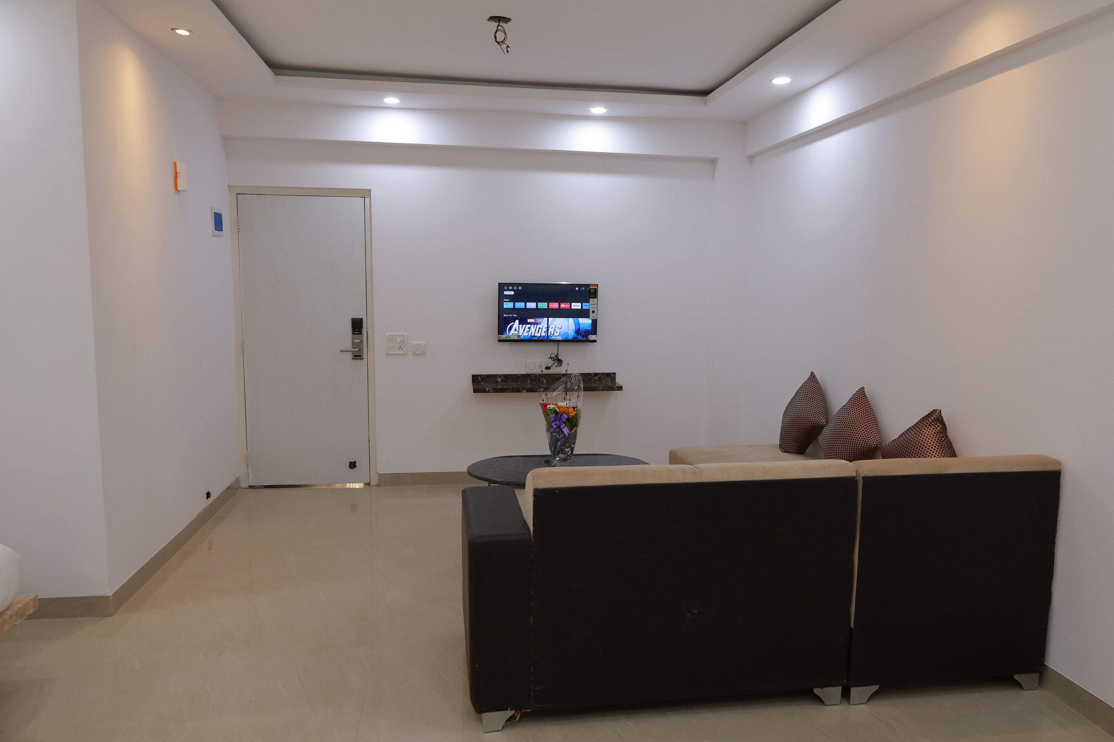 Una sala de estar moderna con un sofá negro, una mesita con un jarrón y un televisor de pantalla plana montado en la pared.