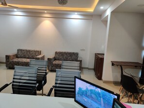 Une pièce moderne et bien éclairée, comprenant un ensemble de canapés, des fauteuils, une petite table et un écran de télévision diffusant un paysage.