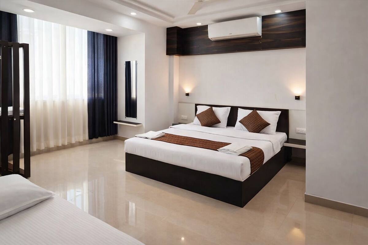 A modern hotel room with a large bed, bedside tables, an air conditioning unit, and a view of the outside through the window.