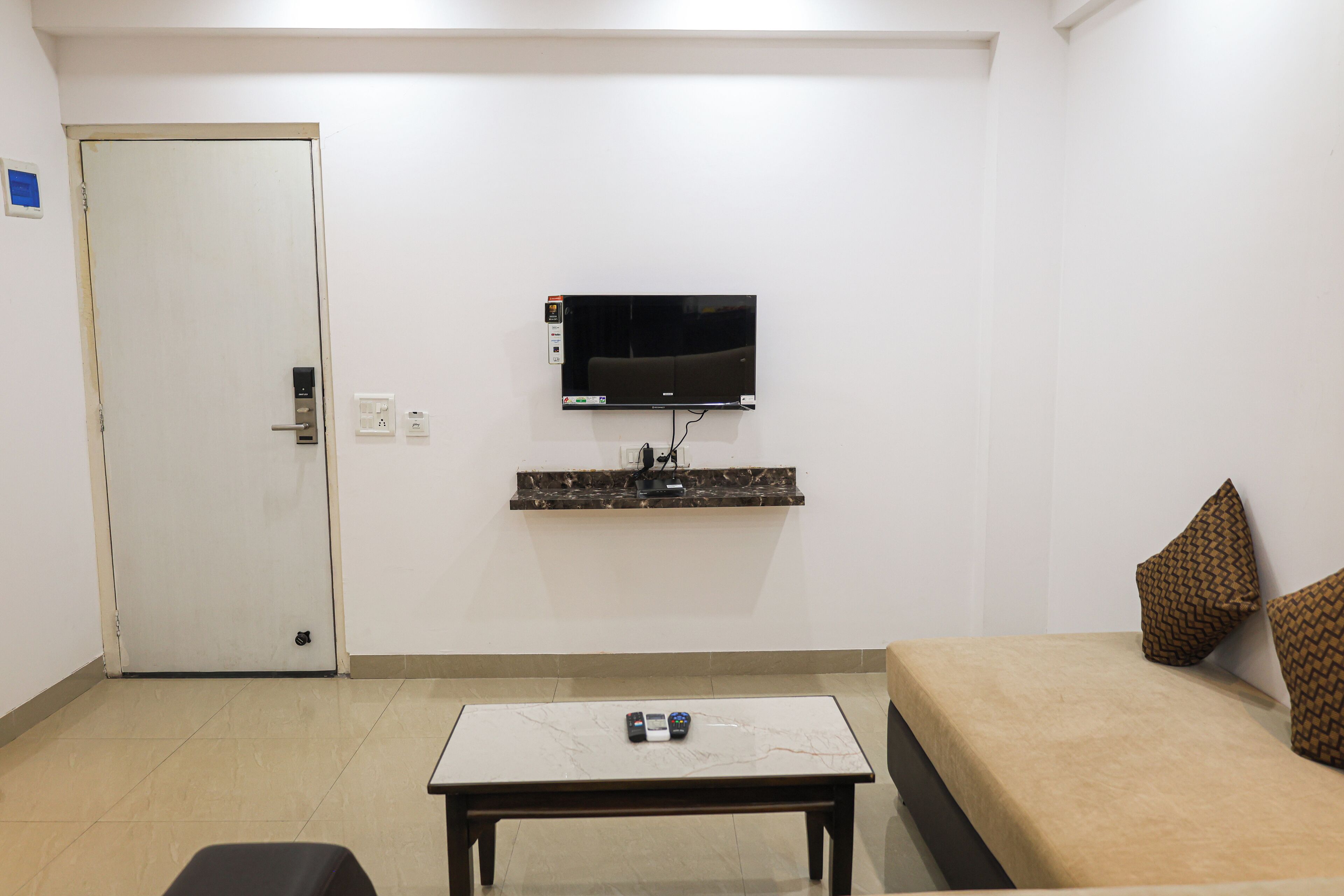 A hotel room with a bed, a TV mounted on the wall, a small table, and a door.