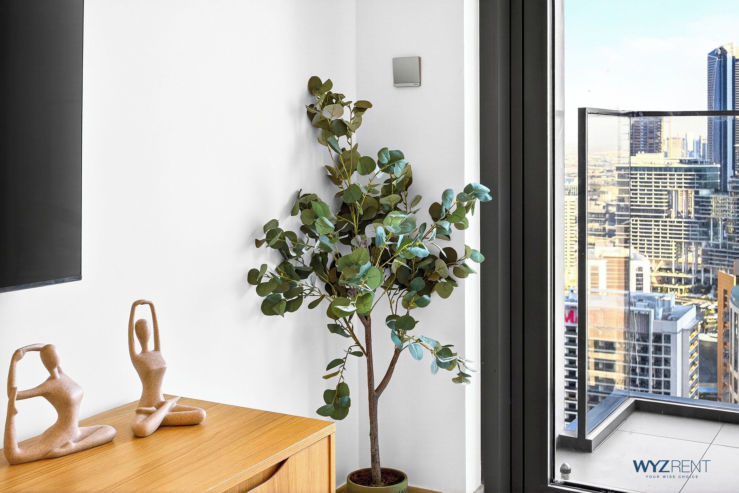 A potted plant with a cityscape view, a wooden desk, and a wall-mounted light switch.