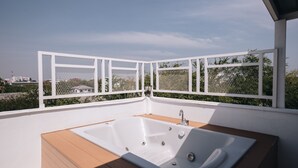 A modern outdoor hot tub with a wooden deck, surrounded by white railings and a clear view of the city skyline. - 2BR with Private Pool and Rooftop Jacuzzi in Huahin Ocean & Mountain View (หัวหิน)