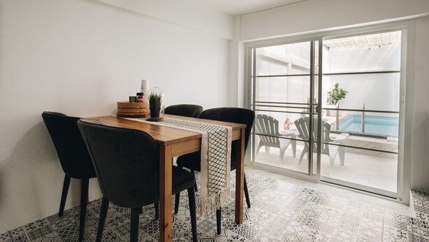 A dining area with a wooden table and black chairs, a small potted plant, and a view of a swimming pool through a glass door. - 2BR with Private Pool and Rooftop Jacuzzi in Huahin Ocean & Mountain View (หัวหิน)