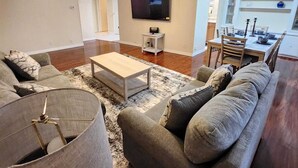 A living room with a sofa, coffee table, and a television on the wall. - Country Home in the City with and Acre of Land (Zephyrhills)