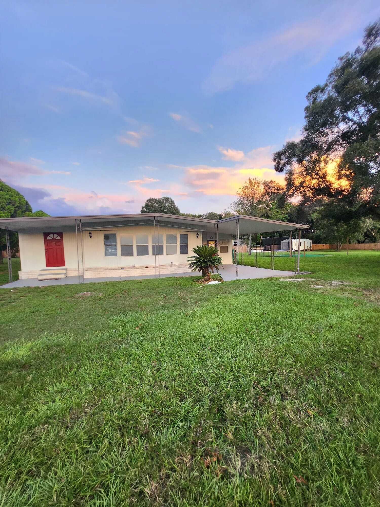 A single-story building with a red door, a covered outdoor area, and a well-maintained lawn.