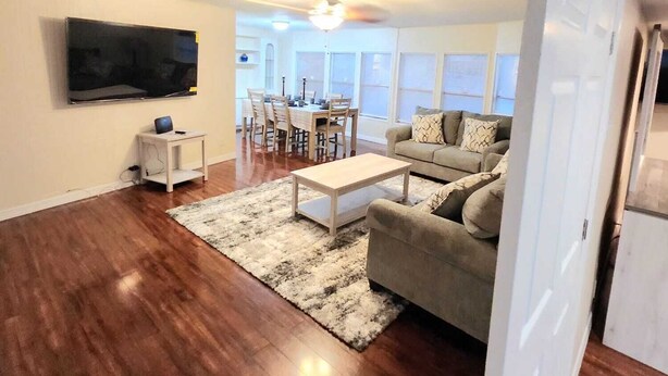 A living room with hardwood flooring, a beige sofa, a coffee table, and a TV mounted on the wall. - Country Home in the City with and Acre of Land (Zephyrhills)