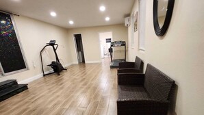 A spacious living area with a large window, a treadmill, a wall-mounted mirror, and a dark-colored sofa. - Country Home in the City with and Acre of Land (Zephyrhills)