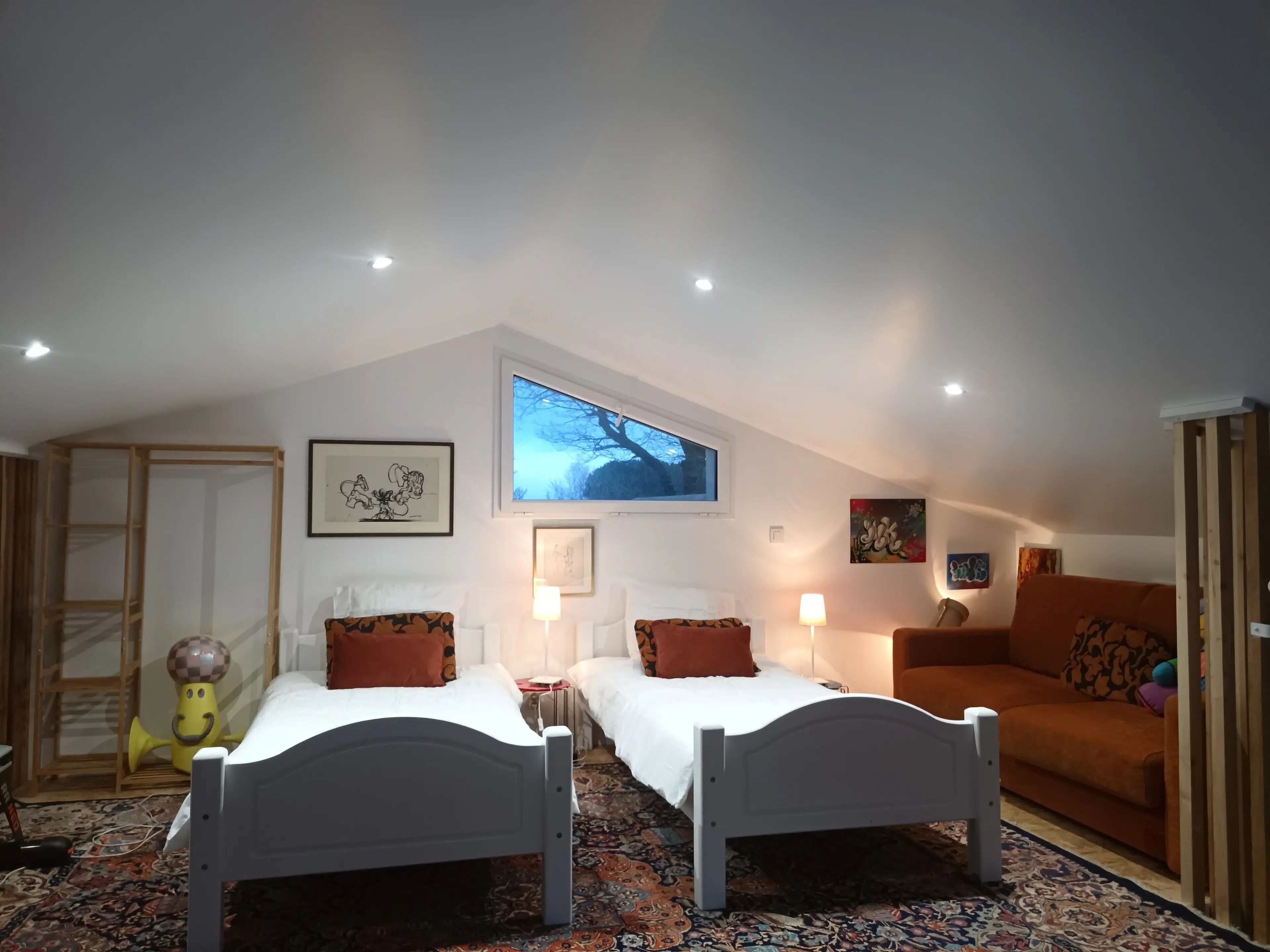A bedroom with two single beds, a sofa, a TV, and artwork on the walls.