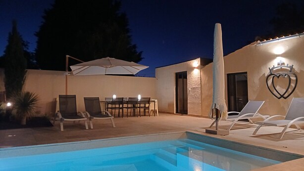 Un espace piscine avec des chaises longues et une table ombragée par des parasols.