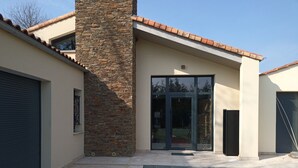 Un bâtiment moderne avec une façade en pierre, de grandes portes vitrées et un toit recouvert de tuiles.