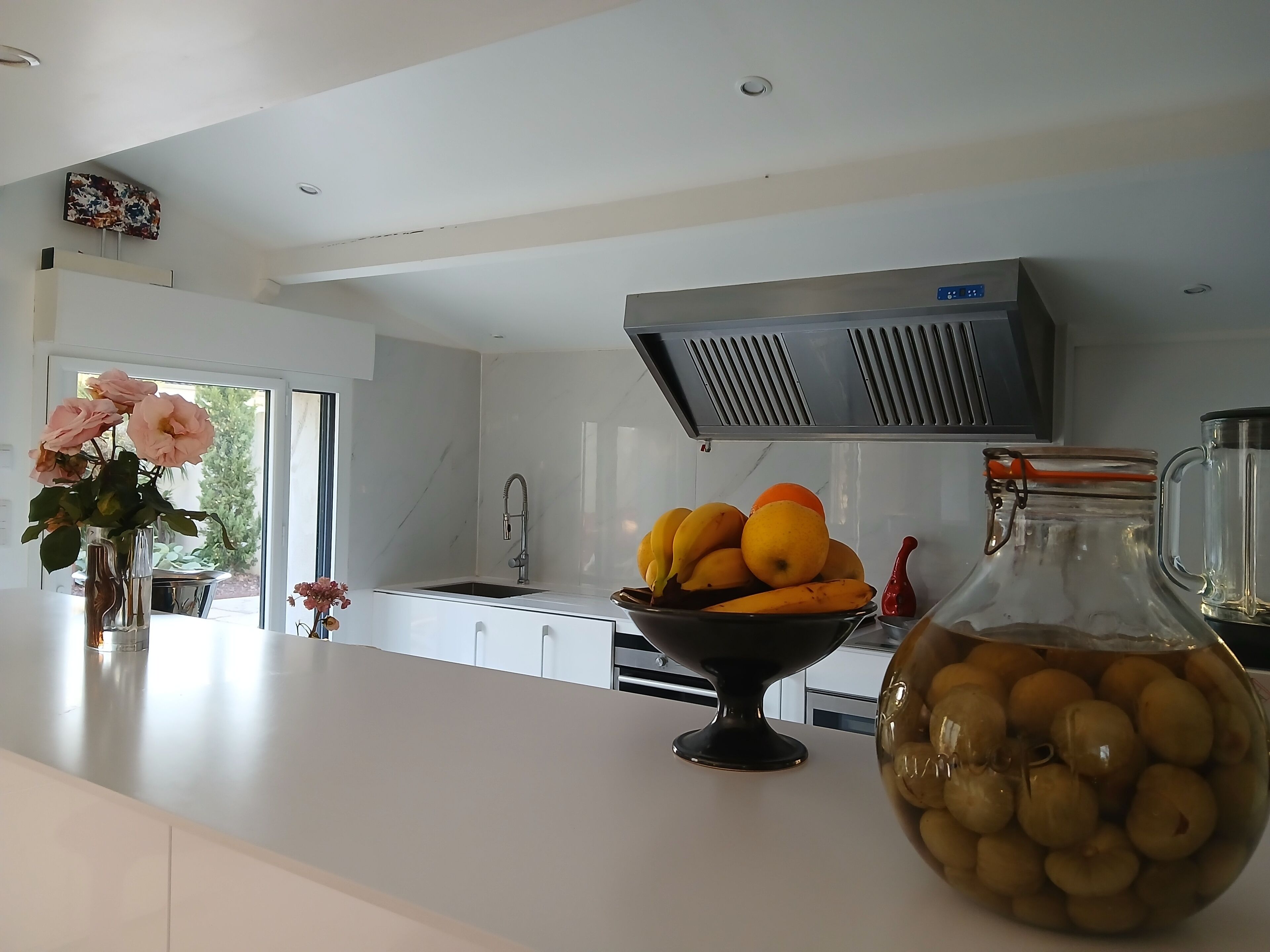 Een moderne keuken met een wit aanrecht, een schaal fruit en een bloemenvaas.