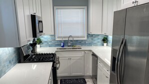 A modern kitchen with white cabinets, a stainless steel refrigerator, a built-in oven, and a window with blinds. - Charming 2-bedroom house with AC, WiFi in delightful Atlanta (Atlanta)