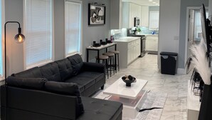 A modern living room with a black leather sofa, a coffee table, and a kitchen in the background. - Charming 2-bedroom house with AC, WiFi in delightful Atlanta (Atlanta)