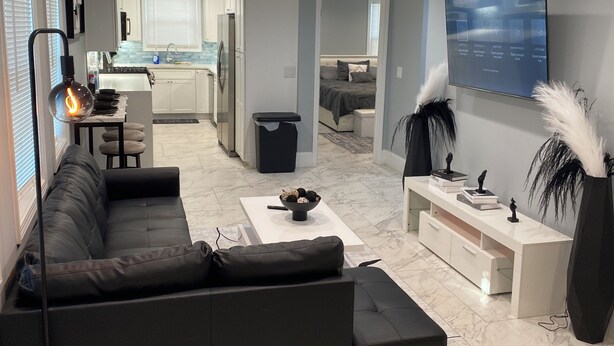A modern living room with a black sectional sofa, a coffee table, and a TV mounted on the wall. - Charming 2-bedroom house with AC, WiFi in delightful Atlanta (Atlanta)