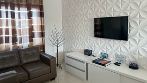 Ein modernes Wohnzimmer mit einer braunen Ledersofa, einer weißen Unterhaltungseinheit mit einem Flachbildfernseher und einem dekorativen Baum.