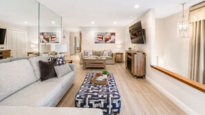 A modern living room with a sofa, ottoman, coffee table, and a TV. - 25% Off Sept 10-12, Walk 2 Beach, Private Jacuzzi! (Oxnard)