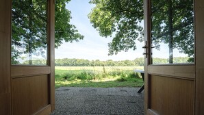 An open wooden door leading to a gravel path with a view of a grassy field and trees. - Attractive Swedish group accommodation by the meadow (Soest)