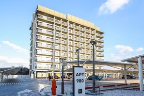 A multi-story residential building with balconies, a parking area, and a sign indicating 'APT 980'. - Modern Studio in MAG City Dubai (Dubai)