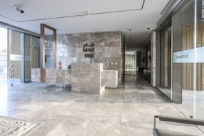 A reception desk with a marble counter, a glass door labeled 'ENTRANCE', and a corridor with a patterned rug. - Modern Studio in MAG City Dubai (Dubai)