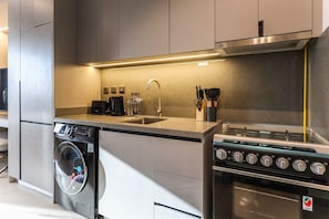 A compact kitchen with a built-in washer, a sink, and a stove. - Modern Studio in MAG City Dubai (Dubai)