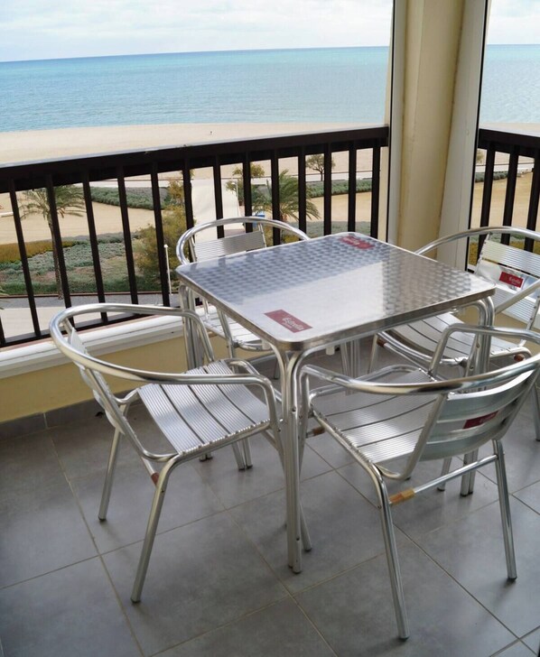 A balcony with a table and chairs, overlooking a beach and the sea.